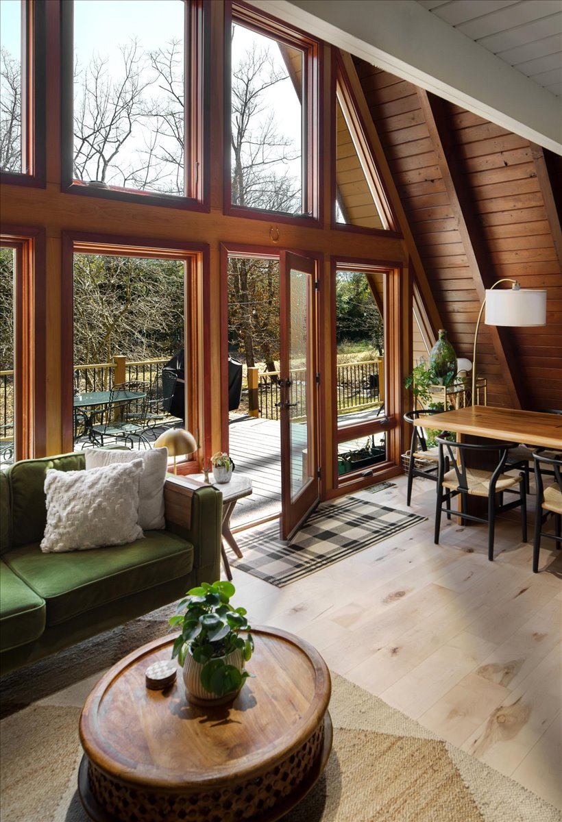 A-frame living room with vaulted wood ceiling, tall windows, green sofa, and round coffee table