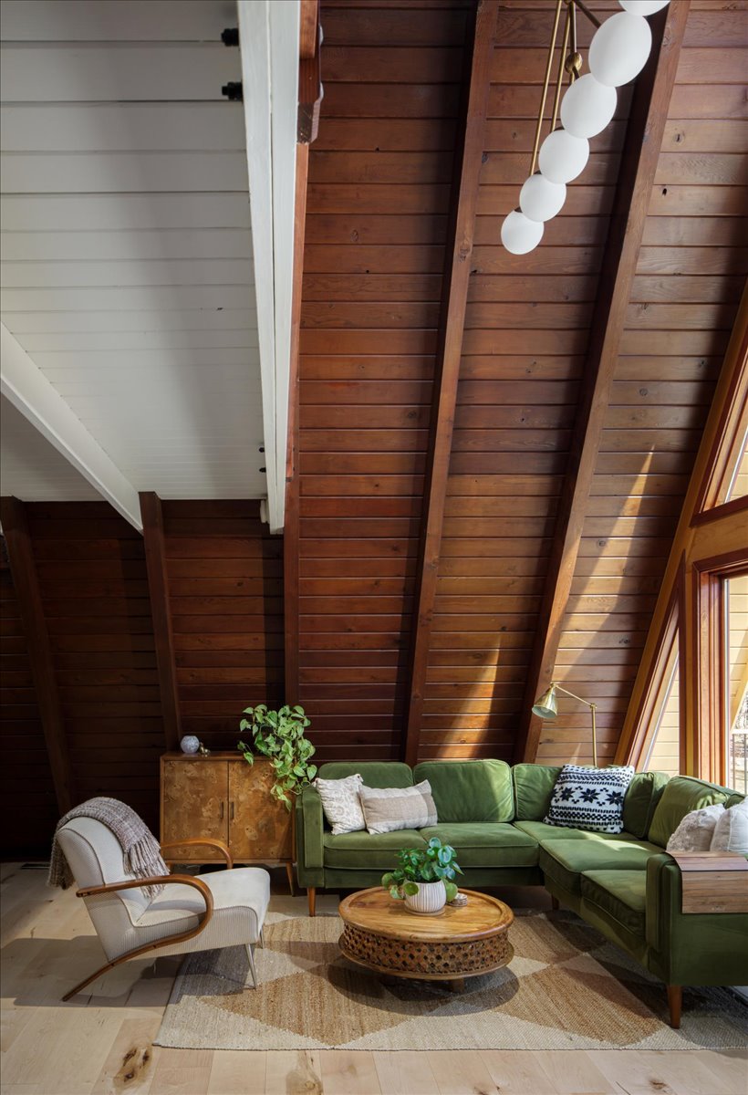 A-frame living room seating area with green sofa, wood ceiling, and globe light fixture