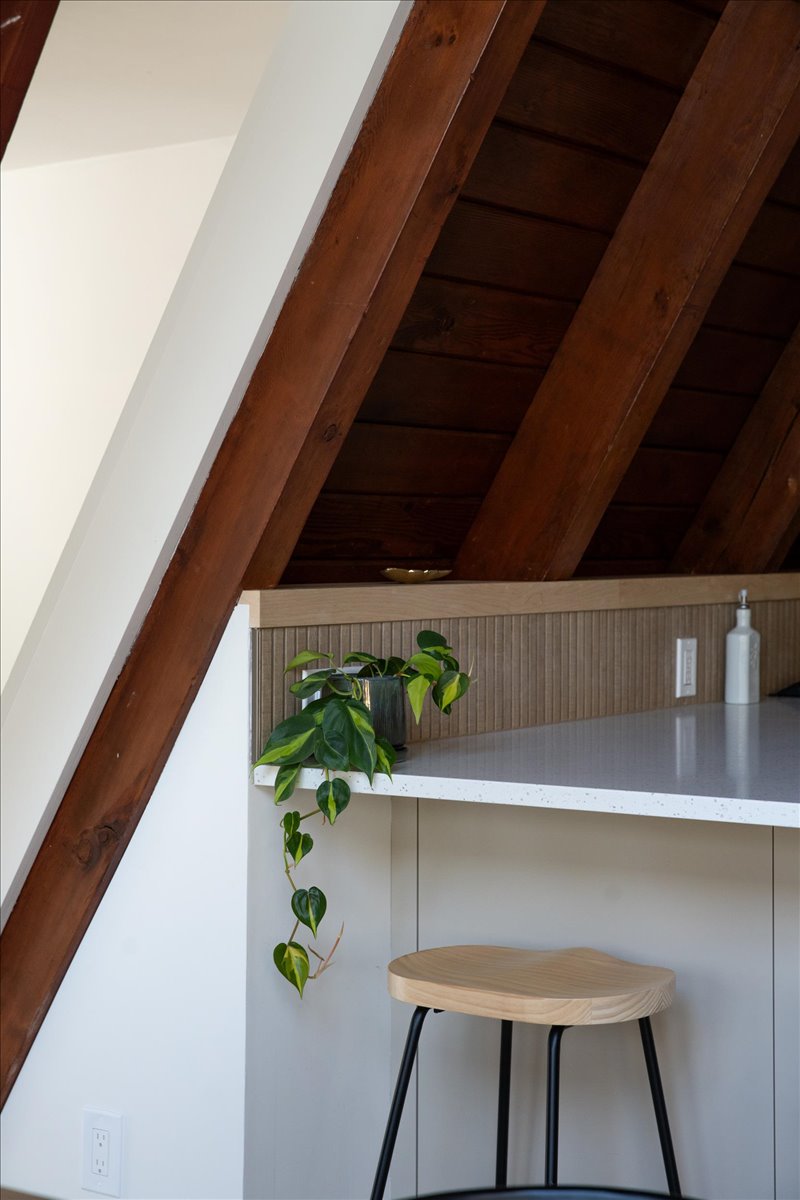 Kitchen counter tucked beneath angled wood wall with stool and trailing plant