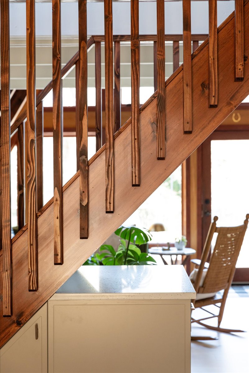 Stained slat railing above white kitchen cabinetry and a plant