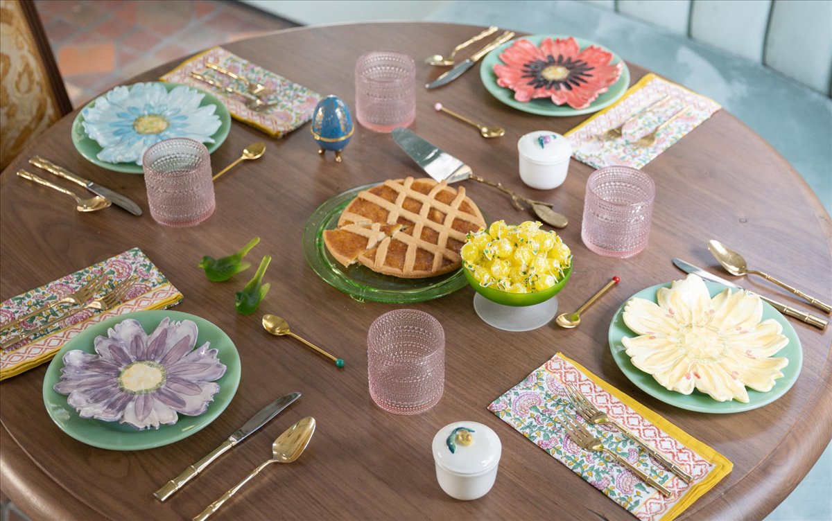 Round table set with flower-shaped plates, patterned linens, brass flatware, and pie