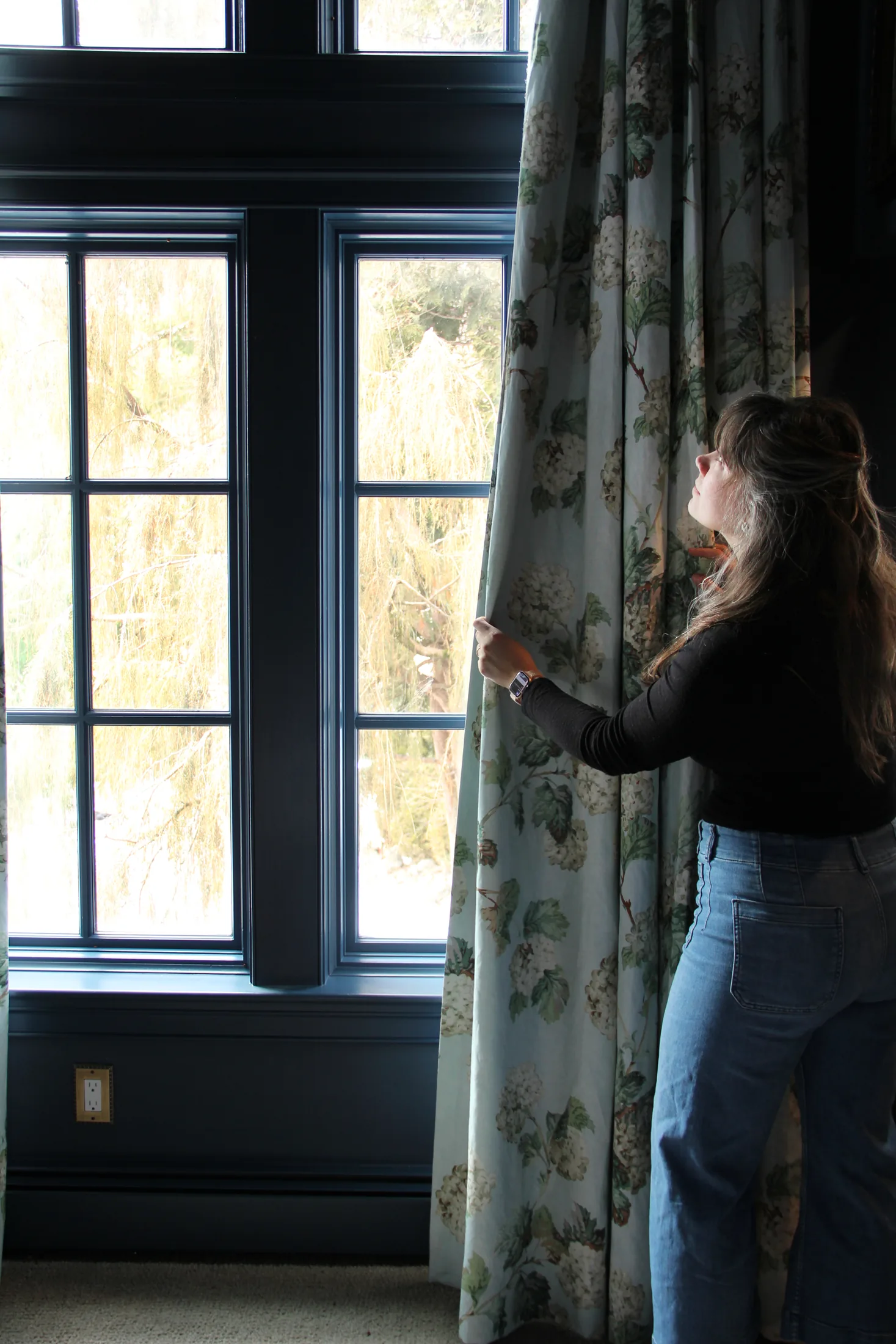 Emeline Tinsman adjusting floral drapery beside black-trimmed windows