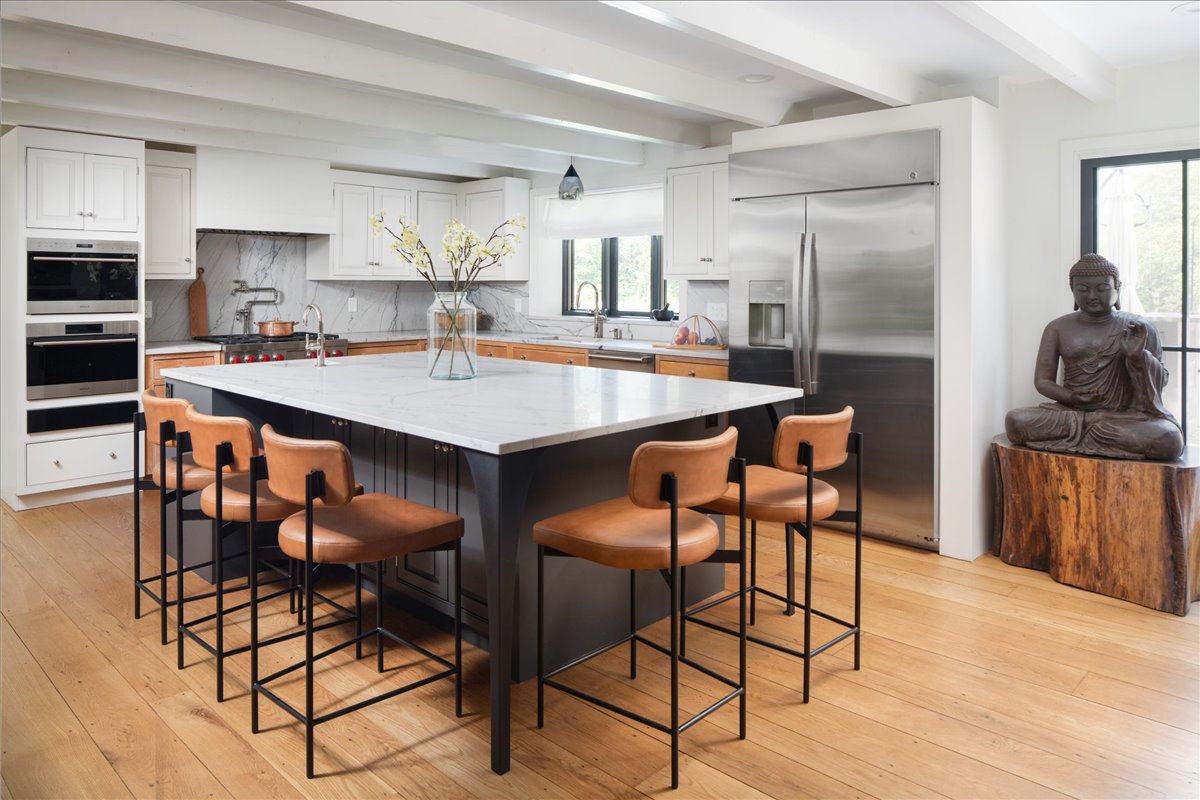 Renovated kitchen with marble counters, panel-front appliances, wood floors, and leather stools
